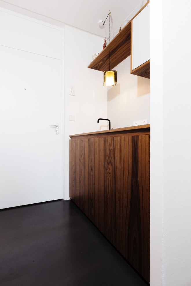 Design ideas for a small midcentury single-wall separate kitchen in Munich with an undermount sink, flat-panel cabinets, dark wood cabinets, solid surface benchtops, grey splashback, black appliances, concrete floors and black floor.