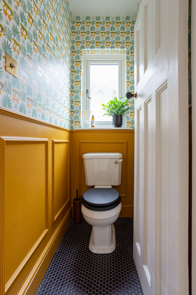 Cette image montre un petit WC et toilettes traditionnel avec un mur orange, un sol noir et du lambris.