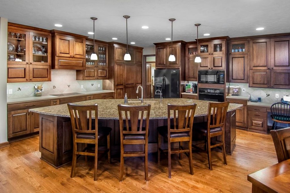 This is an example of a mid-sized arts and crafts l-shaped eat-in kitchen in Omaha with an undermount sink, raised-panel cabinets, dark wood cabinets, granite benchtops, beige splashback, ceramic splashback, black appliances, medium hardwood floors and with island.