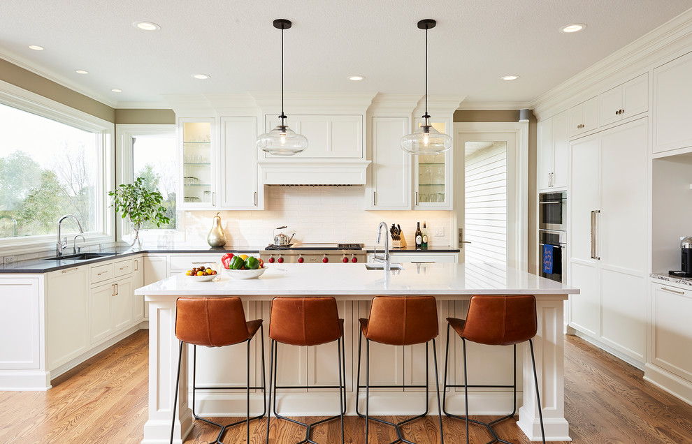 This is an example of a large transitional u-shaped kitchen in Minneapolis with an undermount sink, shaker cabinets, white cabinets, white splashback, panelled appliances, medium hardwood floors, with island, brown floor and black benchtop.