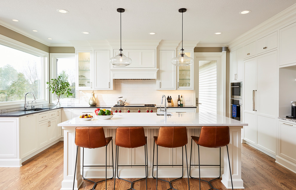 Kitchen - large transitional u-shaped medium tone wood floor and brown floor kitchen idea in Minneapolis with an undermount sink, shaker cabinets, white cabinets, white backsplash, paneled appliances, an island and black countertops