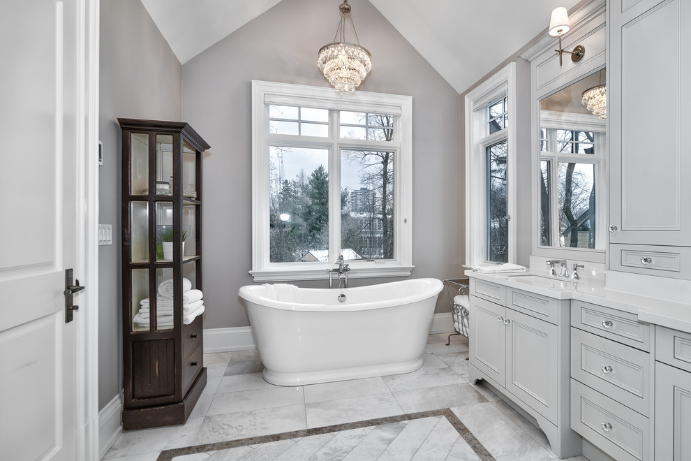 Inspiration for an expansive transitional master bathroom in Toronto with furniture-like cabinets, grey cabinets, a freestanding tub, an alcove shower, a two-piece toilet, grey walls, marble floors, an undermount sink, engineered quartz benchtops, multi-coloured floor, a hinged shower door and grey benchtops.