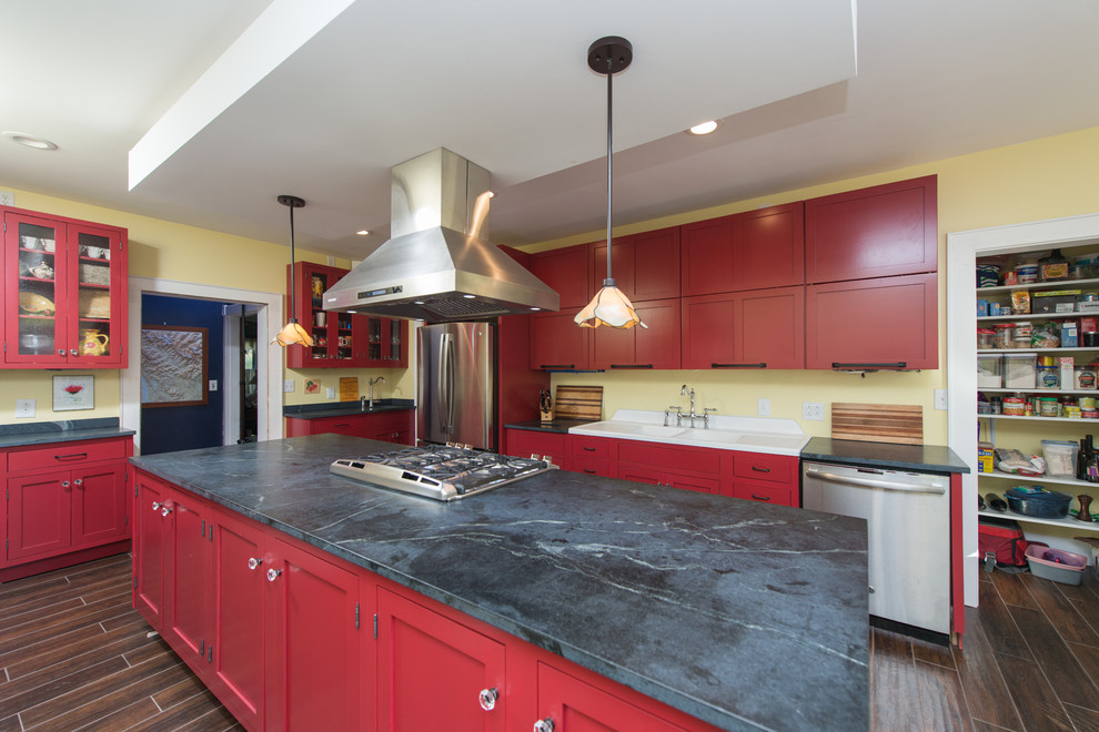 Example of a mid-sized trendy galley dark wood floor and brown floor eat-in kitchen design with a double-bowl sink, raised-panel cabinets, red cabinets, soapstone countertops, stainless steel appliances and an island