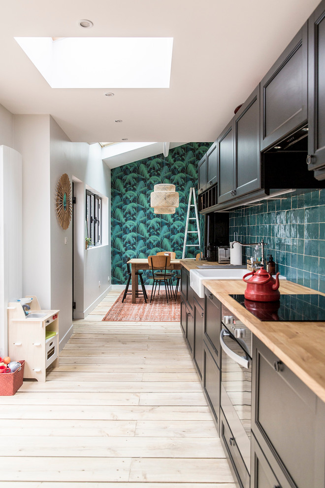 Inspiration for a mid-sized modern single-wall open plan kitchen in Paris with light hardwood floors, a single-bowl sink, wood benchtops, green splashback, ceramic splashback, stainless steel appliances, beaded inset cabinets and brown cabinets.
