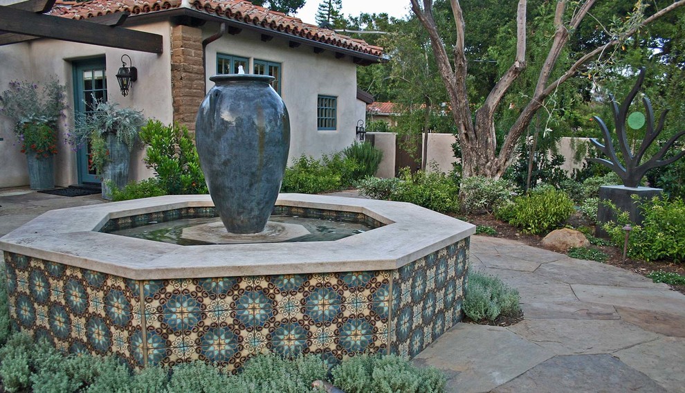 This is an example of a large mediterranean courtyard partial sun formal garden in Santa Barbara with natural stone pavers and a water feature.