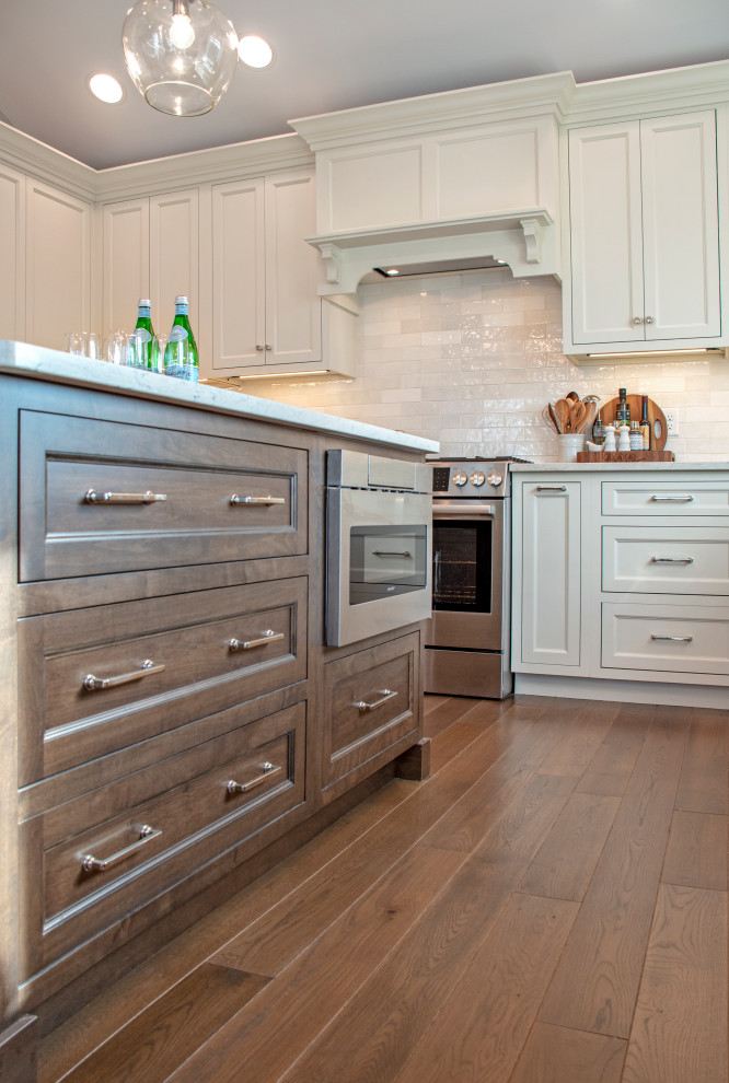Transitional medium tone wood floor and brown floor eat-in kitchen photo with shaker cabinets, white cabinets, quartz countertops, white backsplash, ceramic backsplash, stainless steel appliances, an island and white countertops