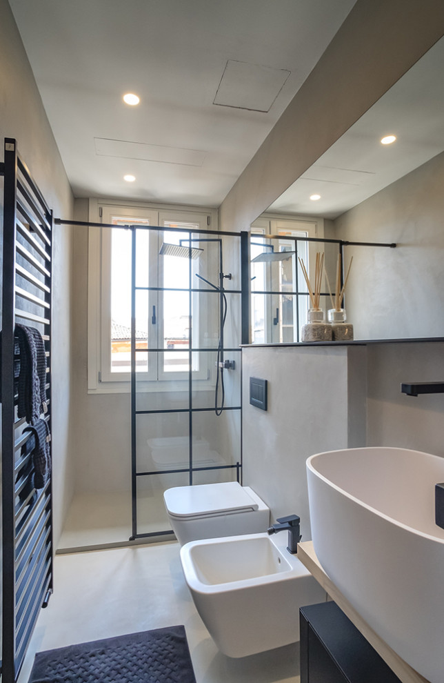 Inredning av ett industriellt litet badrum med dusch, med släta luckor, svarta skåp, en vägghängd toalettstol, grå väggar, betonggolv, ett fristående handfat, träbänkskiva, grått golv och med dusch som är öppen