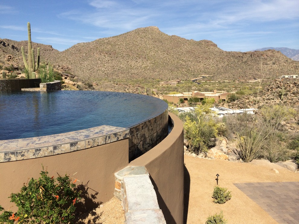 Design ideas for a large contemporary backyard custom-shaped infinity pool in Phoenix with a water feature and natural stone pavers.