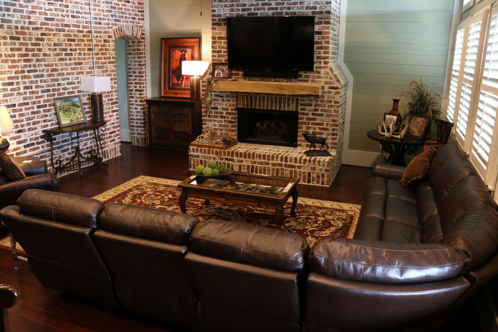 Photo of a large industrial open concept family room in Houston with green walls, medium hardwood floors, a standard fireplace, a brick fireplace surround and a wall-mounted tv.