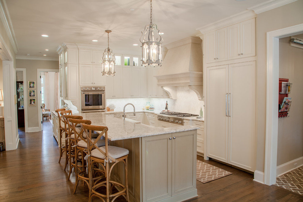 Design ideas for a mid-sized traditional l-shaped open plan kitchen in Nashville with a farmhouse sink, recessed-panel cabinets, white cabinets, quartz benchtops, white splashback, glass tile splashback, panelled appliances, dark hardwood floors and with island.