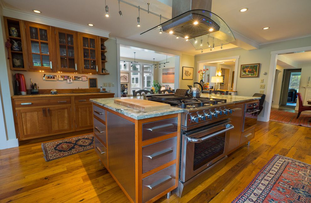 This is an example of a large eclectic l-shaped eat-in kitchen in Burlington with a single-bowl sink, recessed-panel cabinets, medium wood cabinets, granite benchtops, multi-coloured splashback, ceramic splashback, medium hardwood floors and with island.