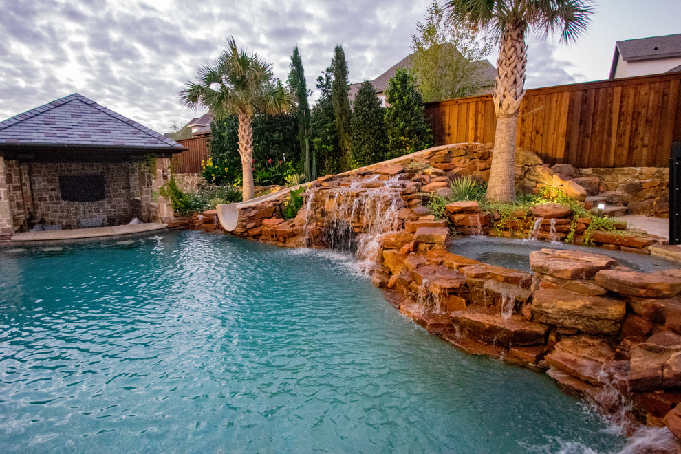 This is an example of a mid-sized tropical backyard custom-shaped pool in Dallas with a water slide and natural stone pavers.