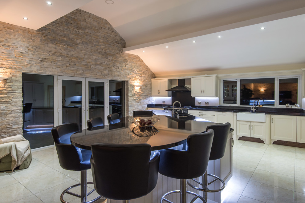 Design ideas for an expansive classic l-shaped open plan kitchen in Belfast with a belfast sink, beaded cabinets, white cabinets, granite worktops, black splashback, stone slab splashback, black appliances, porcelain flooring, multiple islands, white floors and black worktops.