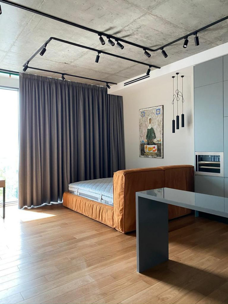 Modelo de dormitorio principal industrial pequeño con paredes beige, suelo de madera clara y suelo naranja