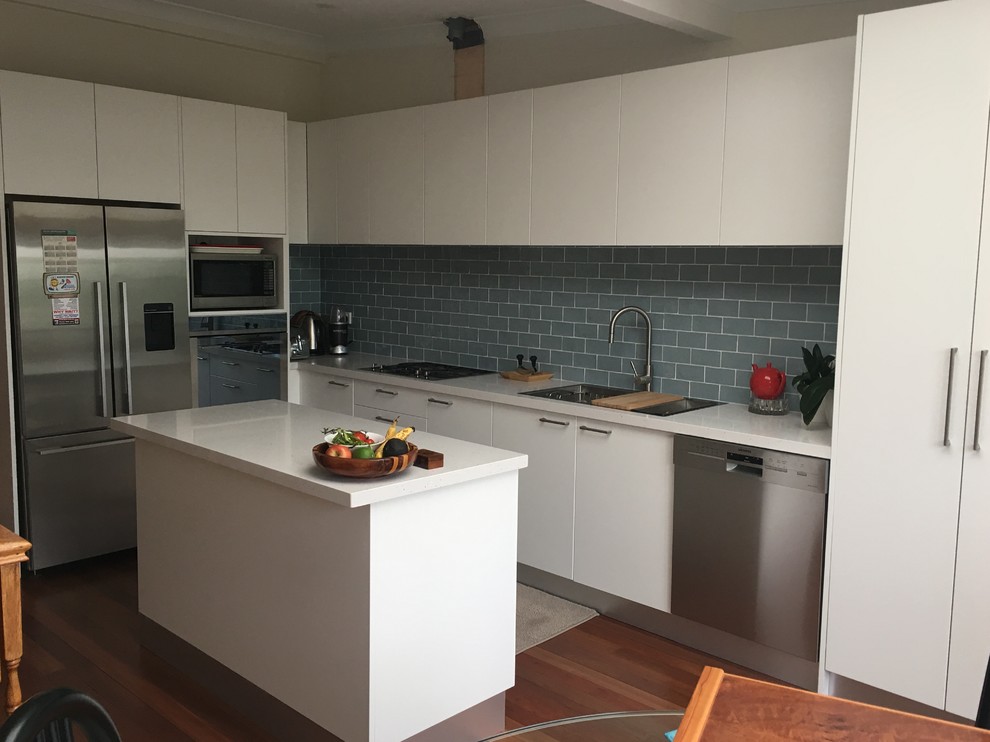 This is an example of a contemporary kitchen pantry in Sydney with a double-bowl sink, white cabinets, grey splashback, subway tile splashback, stainless steel appliances, medium hardwood floors and with island.