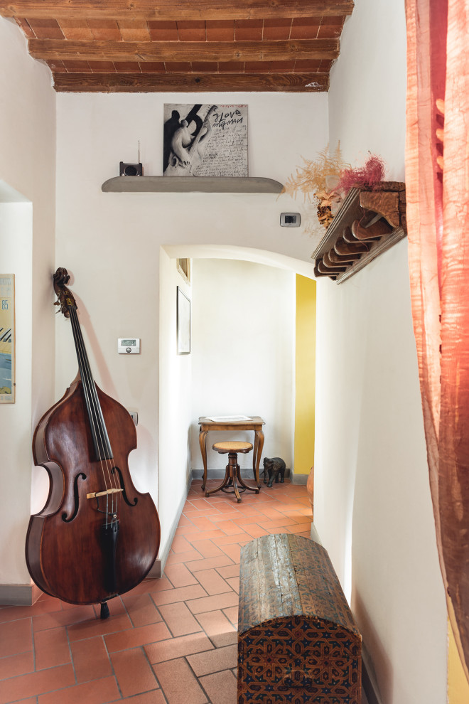 Aménagement d'un petit hall d'entrée moderne avec un mur blanc, tomettes au sol, une porte double, une porte métallisée, un sol rouge et poutres apparentes.