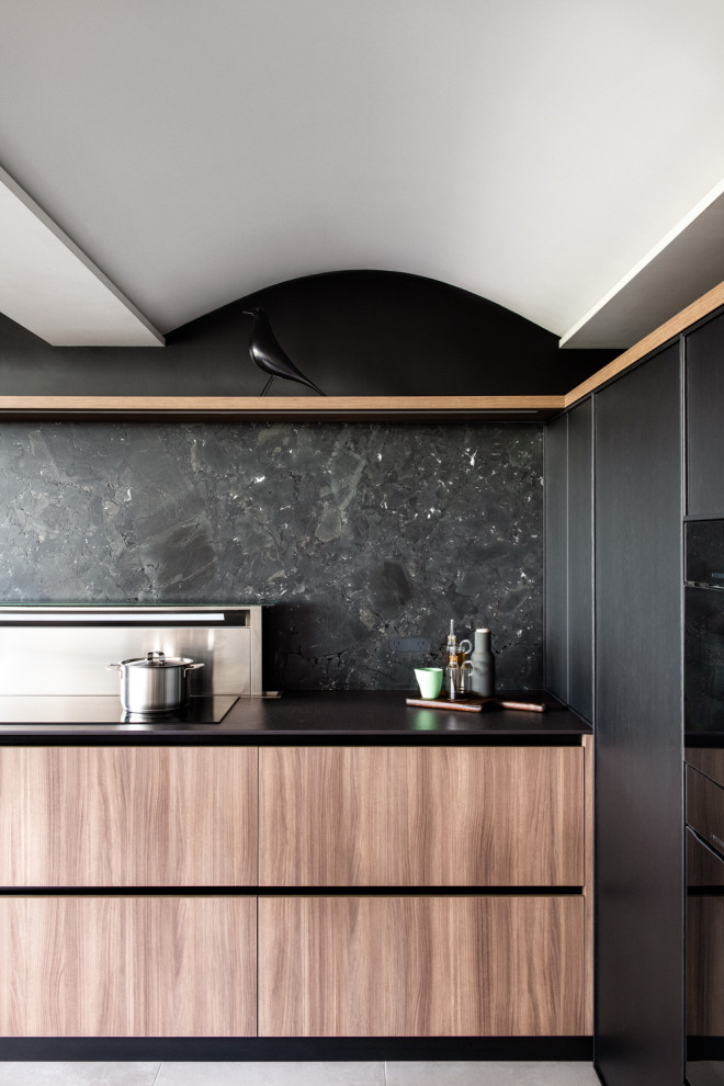 Mid-sized modern u-shaped open plan kitchen in Sydney with an undermount sink, recessed-panel cabinets, black splashback, stone slab splashback, black appliances, porcelain floors, with island, black benchtop and wood.