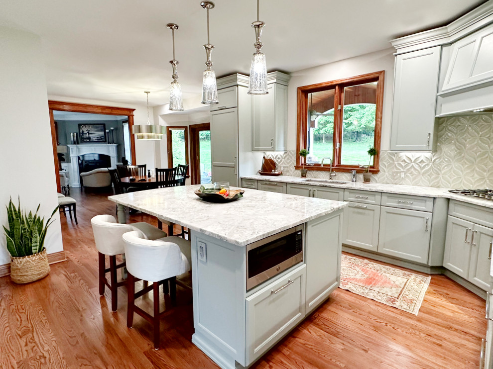 Transitional l-shaped medium tone wood floor eat-in kitchen photo with shaker cabinets, green cabinets, quartzite countertops, porcelain backsplash, paneled appliances and an island