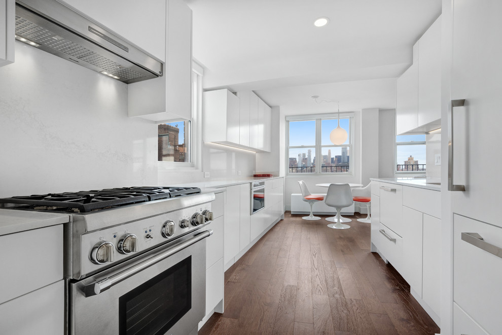 Inspiration for a mid-sized contemporary galley eat-in kitchen in New York with dark hardwood floors, brown floor, flat-panel cabinets, white cabinets, white splashback, stainless steel appliances, no island and white benchtop.