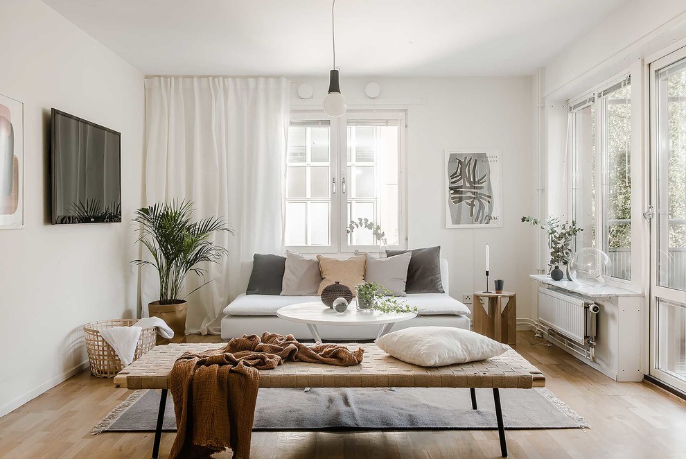 Mid-sized scandinavian enclosed living room in Stockholm with white walls, light hardwood floors, no fireplace and a wall-mounted tv.