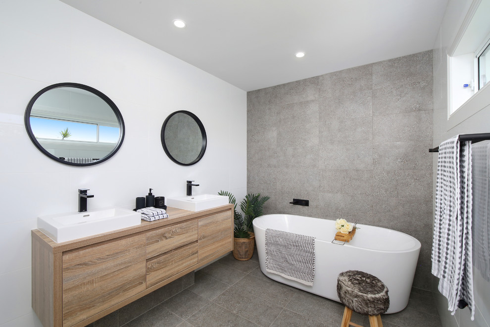 Photo of a beach style bathroom in Sydney with flat-panel cabinets, medium wood cabinets, a freestanding tub, gray tile, white walls, a vessel sink, wood benchtops, grey floor and brown benchtops.