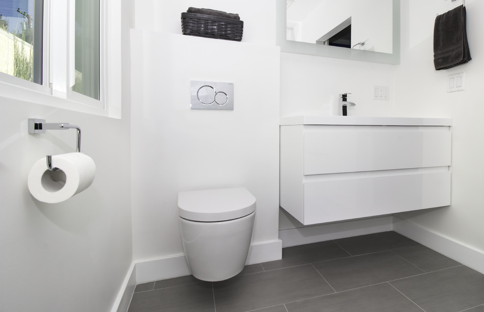 Mid-sized modern 3/4 bathroom in Los Angeles with flat-panel cabinets, white cabinets, a curbless shower, a wall-mount toilet, white tile, porcelain tile, white walls, porcelain floors, an integrated sink, solid surface benchtops, grey floor and an open shower.