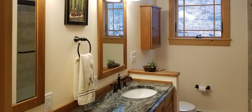This is an example of a small arts and crafts master bathroom in Boston with shaker cabinets, medium wood cabinets, an alcove tub, a shower/bathtub combo, a two-piece toilet, yellow walls, ceramic floors, an undermount sink, granite benchtops, multi-coloured floor, a sliding shower screen and green benchtops.