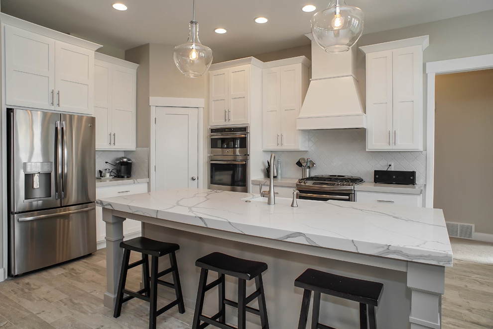 Photo of a mid-sized contemporary l-shaped eat-in kitchen in Salt Lake City with a farmhouse sink, shaker cabinets, white cabinets, marble benchtops, pink splashback, glass tile splashback, stainless steel appliances, light hardwood floors, with island and beige floor.