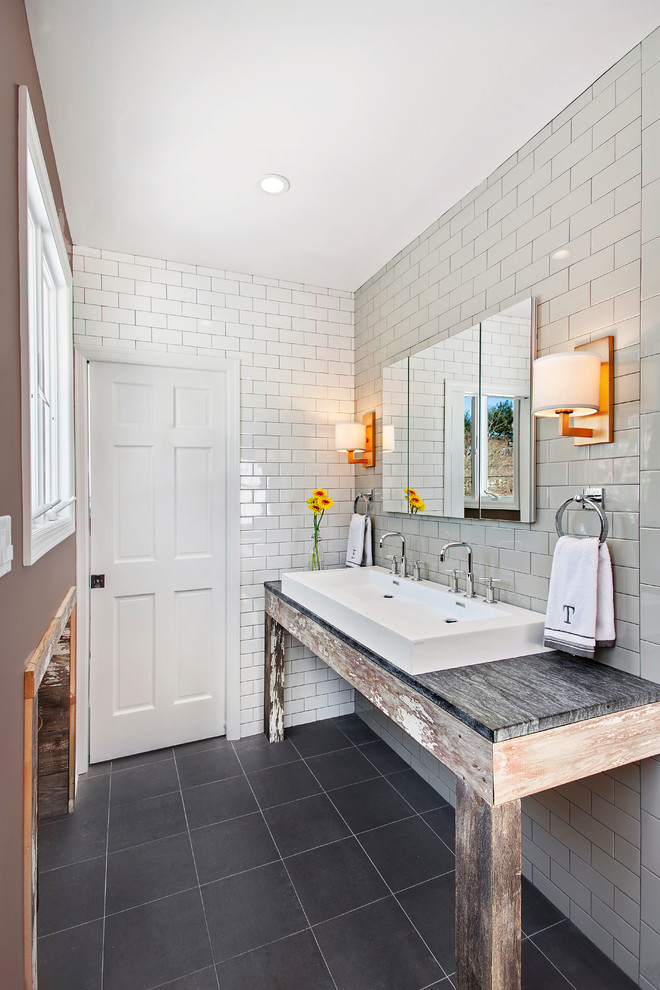 Inspiration for a mid-sized country master bathroom in New York with a trough sink, distressed cabinets, soapstone benchtops, an alcove shower, a one-piece toilet, gray tile, subway tile, white walls and porcelain floors.