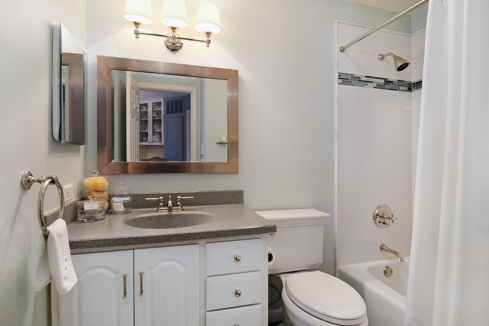 This is an example of a traditional bathroom in New York with an integrated sink, raised-panel cabinets, white cabinets, solid surface benchtops, an alcove tub, a shower/bathtub combo, a two-piece toilet, white tile and ceramic tile.