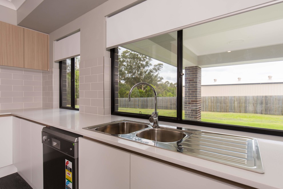 Photo of a large country galley open plan kitchen in Brisbane with a double-bowl sink, flat-panel cabinets, light wood cabinets, solid surface benchtops, beige splashback, subway tile splashback, stainless steel appliances, vinyl floors, with island, black floor and white benchtop.