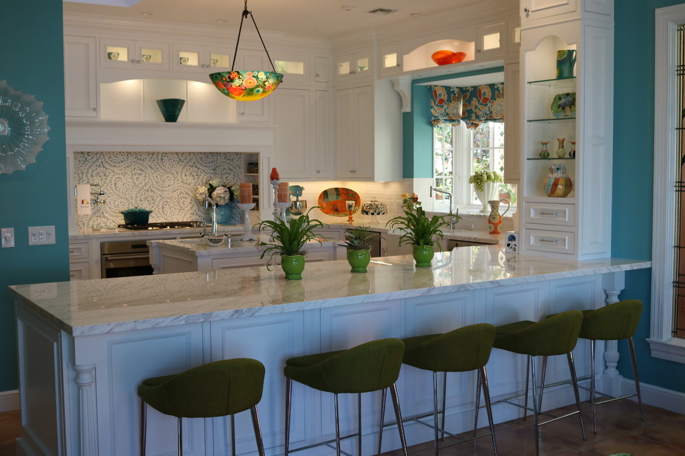 Design ideas for a large beach style u-shaped open plan kitchen in Miami with a farmhouse sink, recessed-panel cabinets, white cabinets, marble benchtops, white splashback, mosaic tile splashback, stainless steel appliances, porcelain floors and with island.