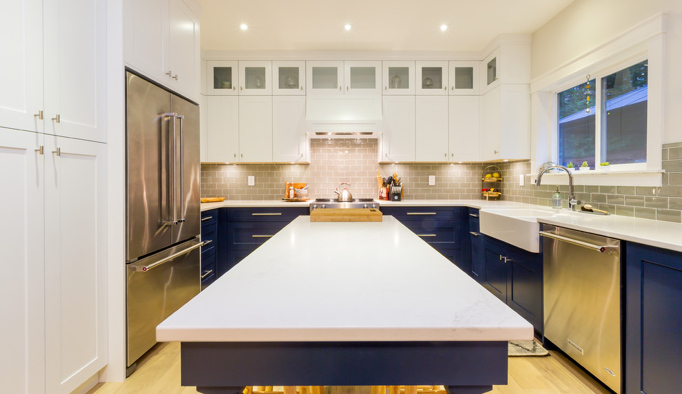 Open concept kitchen - large transitional u-shaped light wood floor open concept kitchen idea with a farmhouse sink, shaker cabinets, blue cabinets, quartz countertops, gray backsplash, glass tile backsplash, stainless steel appliances, an island and white countertops
