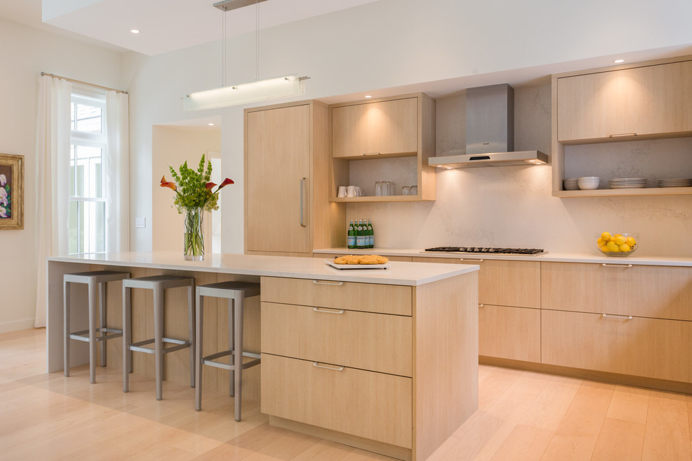 Large contemporary l-shaped eat-in kitchen in Portland Maine with a drop-in sink, flat-panel cabinets, light wood cabinets, quartz benchtops, multi-coloured splashback, stainless steel appliances, light hardwood floors, with island and beige floor.