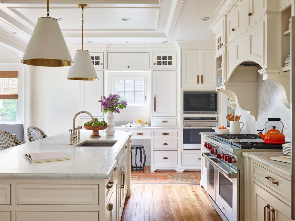 Example of a large classic single-wall medium tone wood floor and brown floor enclosed kitchen design in Boston with an undermount sink, beaded inset cabinets, white cabinets, marble countertops, white backsplash, marble backsplash, paneled appliances, an island and gray countertops
