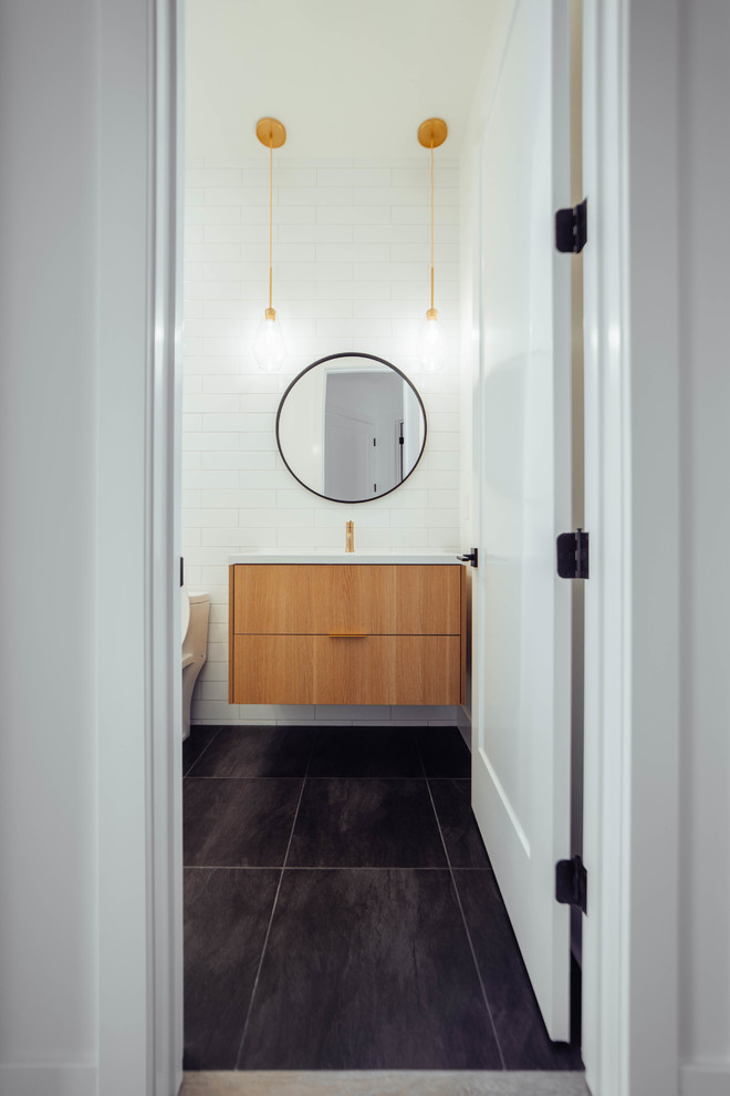 Inspiration for a mid-sized contemporary powder room in Sacramento with flat-panel cabinets, medium wood cabinets, a one-piece toilet, white tile, subway tile, white walls, porcelain floors, an undermount sink, engineered quartz benchtops, black floor and white benchtops.