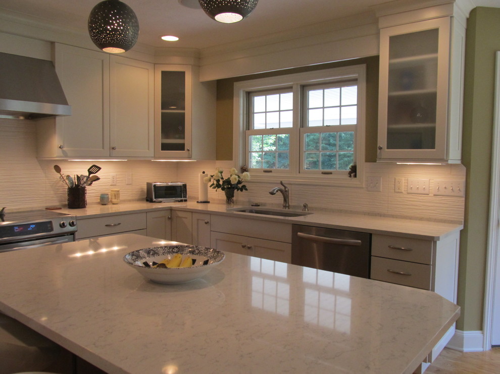 Transitional l-shaped medium tone wood floor open concept kitchen photo with an undermount sink, recessed-panel cabinets, white cabinets, quartz countertops, white backsplash, ceramic backsplash, stainless steel appliances and an island