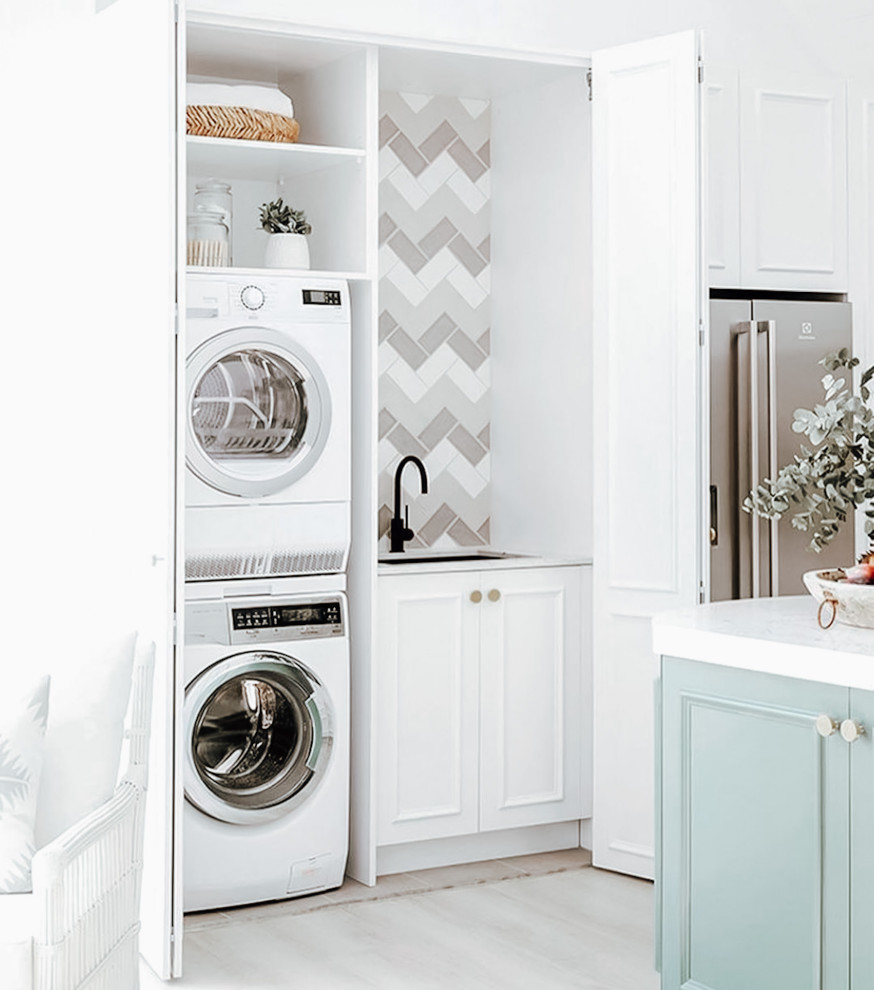 Inspiration for a small single-wall laundry cupboard in Dallas with an undermount sink, white cabinets, quartzite benchtops, grey splashback, ceramic splashback, white walls, light hardwood floors, a stacked washer and dryer, grey floor and white benchtop.