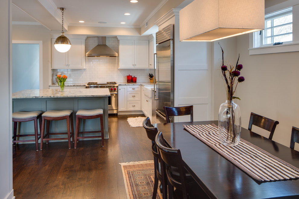 Mid-sized transitional l-shaped eat-in kitchen in Minneapolis with a farmhouse sink, shaker cabinets, white cabinets, granite benchtops, white splashback, subway tile splashback, stainless steel appliances, dark hardwood floors and with island.