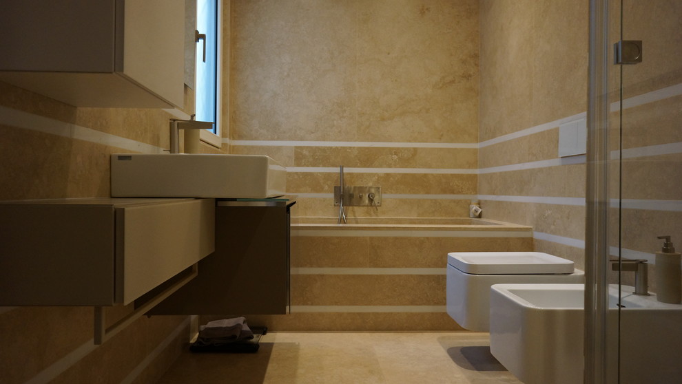 Small modern 3/4 bathroom in Rome with flat-panel cabinets, brown cabinets, a drop-in tub, a double shower, a wall-mount toilet, yellow tile, travertine, travertine floors, a trough sink, glass benchtops, yellow floor, a hinged shower door and yellow walls.