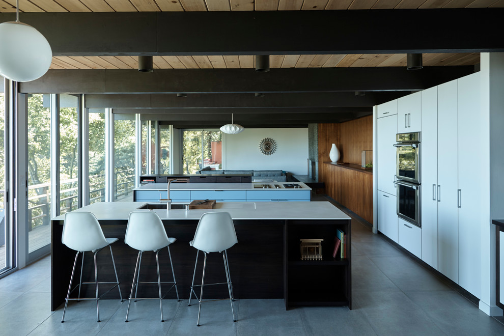 This is an example of a mid-sized midcentury open plan kitchen in San Francisco with flat-panel cabinets, dark wood cabinets, solid surface benchtops, ceramic floors and multiple islands.
