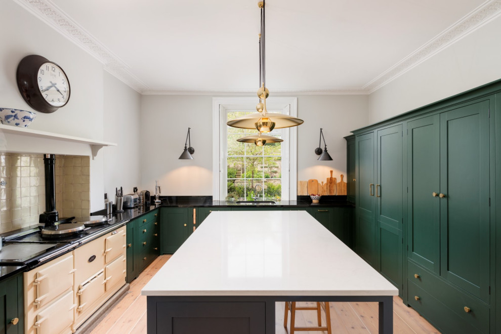 Photo of a transitional u-shaped kitchen in Devon with an undermount sink, shaker cabinets, green cabinets, grey splashback, coloured appliances, light hardwood floors, with island and black benchtop.