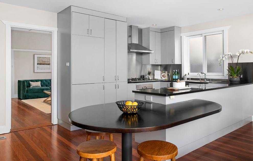 Mid-sized transitional u-shaped open plan kitchen in Sydney with a double-bowl sink, grey cabinets, granite benchtops, stainless steel appliances, medium hardwood floors and black benchtop.