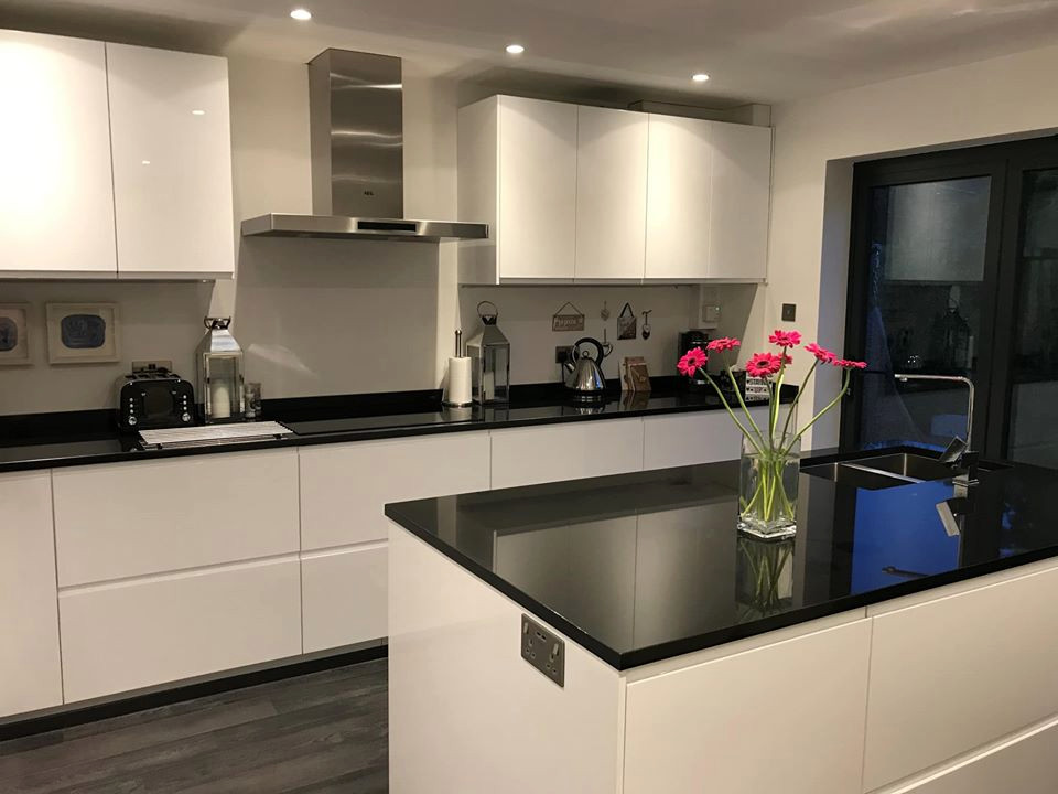 Photo of a modern single-wall kitchen in West Midlands with an undermount sink, white cabinets, with island, black benchtop and granite benchtops.