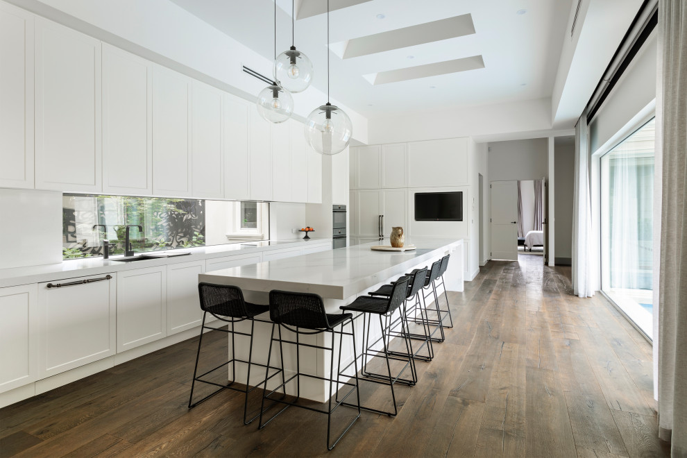 Photo of a contemporary l-shaped kitchen in Melbourne with an undermount sink, shaker cabinets, white cabinets, window splashback, dark hardwood floors, with island, brown floor and white benchtop.