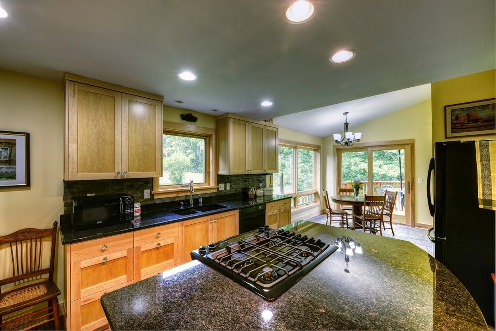 Mid-sized arts and crafts l-shaped eat-in kitchen photo with a double-bowl sink, shaker cabinets, light wood cabinets, granite countertops, gray backsplash, stone tile backsplash, black appliances, an island and black countertops