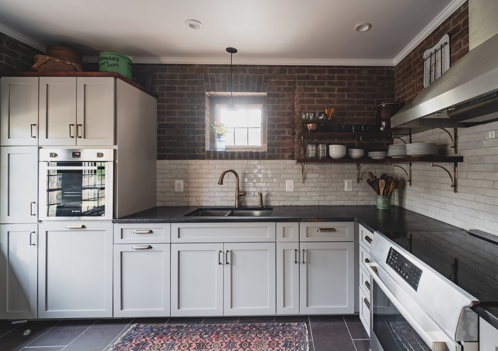 This is an example of a small country l-shaped separate kitchen in Philadelphia with a double-bowl sink, shaker cabinets, grey cabinets, soapstone benchtops, white splashback, terra-cotta splashback, stainless steel appliances, slate floors, no island, purple floor and black benchtop.