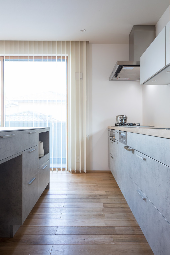 This is an example of a scandinavian single-wall open plan kitchen with an undermount sink, beaded inset cabinets, medium wood cabinets, white splashback, stainless steel appliances, with island, brown floor and grey benchtop.