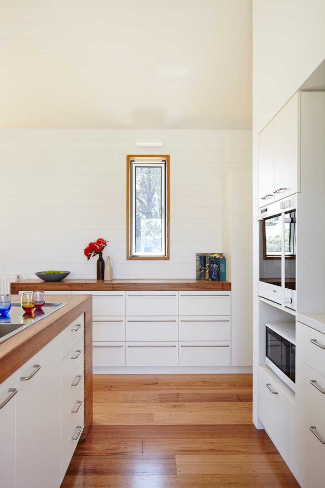 Eat-in kitchen in Geelong with a double-bowl sink, light wood cabinets, wood benchtops, stone slab splashback, white appliances, light hardwood floors and with island.