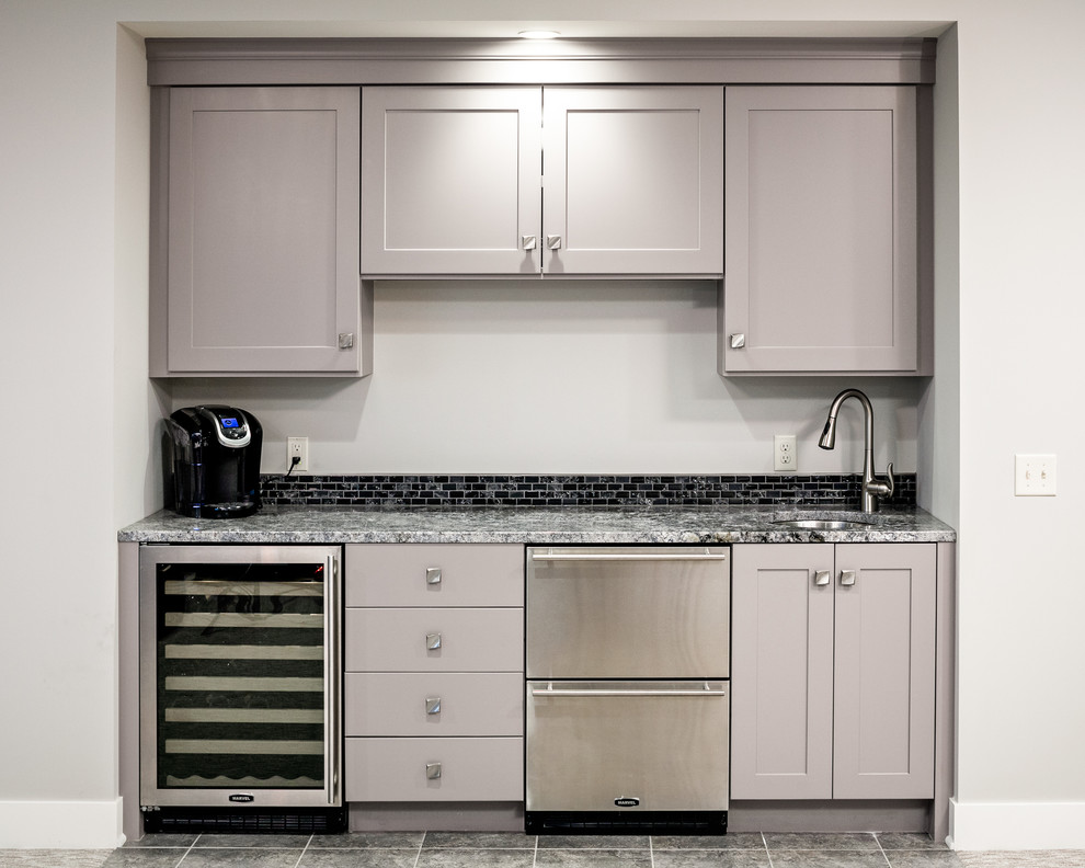 This is an example of a mid-sized modern single-wall wet bar in Grand Rapids with an undermount sink, recessed-panel cabinets, grey cabinets, quartz benchtops, black splashback, ceramic splashback, ceramic floors, grey floor and multi-coloured benchtop.